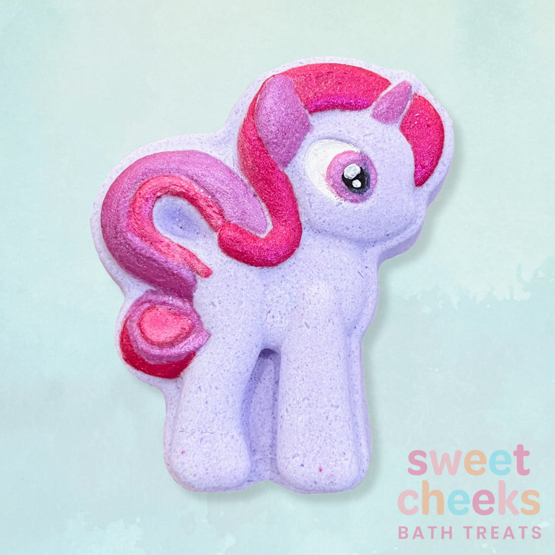 Purple pony shaped bath bomb with pink hair on a light blue background, branded 'sweet cheeks bath treats'.