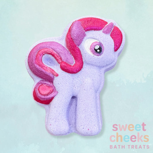 Purple pony shaped bath bomb with pink hair on a light blue background, branded 'sweet cheeks bath treats'.