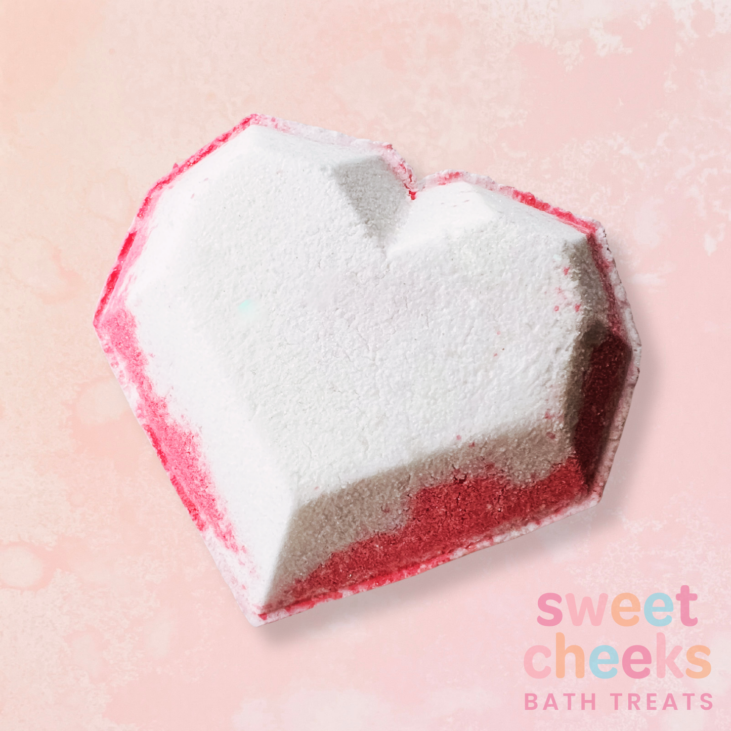 Heart-shaped bath bomb with red and white colors on a pink background, featuring 'sweet cheeks bath treats' branding. Scented with strawberries and cream fragrance.